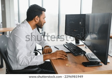 Side view of smart Indian crypto trader, investor, analyst broker, using laptop and smartphone analyzing digital cryptocurrency exchange, stock market charts, thinking of investing and funds risks