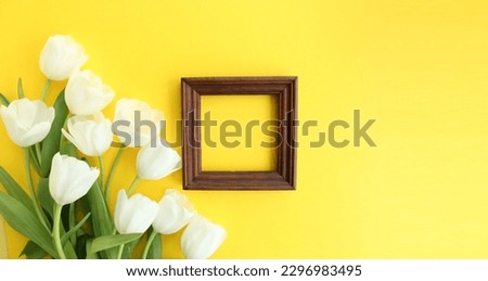 An empty wooden frame with white tulips on yellow background. Perfect for clients' design projects. The flowers are located on the left side of the photo, adding a touch of elegance to any design.