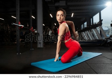 athletic woman in red sportswear sitting on yoga matte in black gym and warming up, girl doing yoga and stretching, attractive woman in fitness club doing flexibility exercise Royalty-Free Stock Photo #2296984851