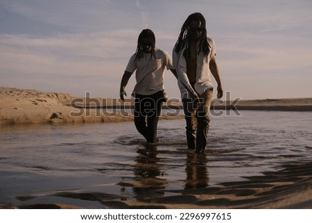 Two african men friends music band wearing dreadlocks posing during sunset standing in water on ocean 