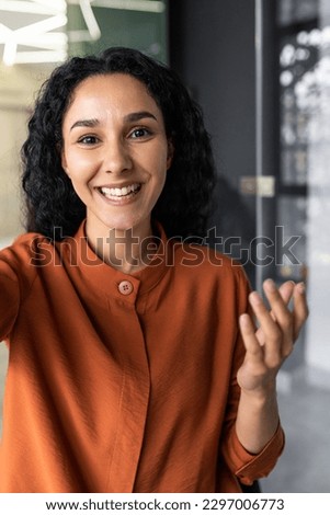 Vertical shot, video call from office hispanic business woman working inside modern office building, talking remotely with friends using app on phone for video call Royalty-Free Stock Photo #2297006773