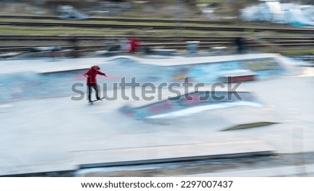 boy in red jacket practicing tricks in skatepart in motion blur in city berlin, germany