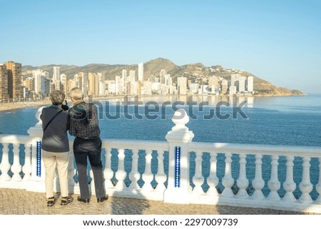 Unrecognizable senior couple with smartphone taking photo of beautiful Benidorm city views and Mediterranean sea