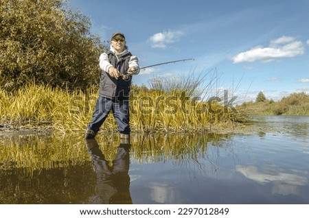 Angler stands in the water and casts a spinning rod. Royalty-Free Stock Photo #2297012849
