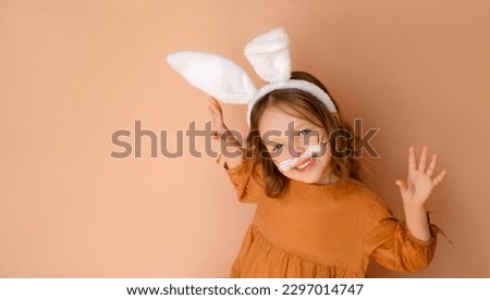 A very beautiful sweet girl in an Easter bunny costume with her arms outstretched looks in amazement at the frame. Aquagrim, body art and face paints Royalty-Free Stock Photo #2297014747