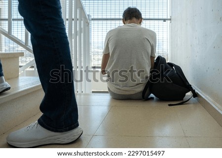 Sad teenage boy with mobile phone and backpack sitting on stairs. Teenager surfing on Internet, watching video, using app. Education, learning difficulties, mobile addiction concept Royalty-Free Stock Photo #2297015497