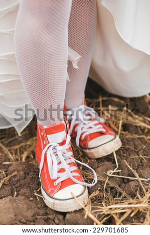 bride in dress in dirty red plimsolls on ground with dry grass