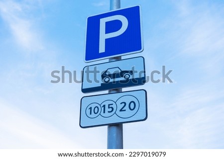 A grey post with several parking signs including a white letter "P" in a blue square, a sign for parking spots, and a sign for paid parking, all set against a beautiful blue sky