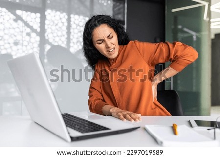 Office worker Latin American business reaper is sick at the workplace, an overtired businesswoman has back pain, massages her back with her hand Royalty-Free Stock Photo #2297019589