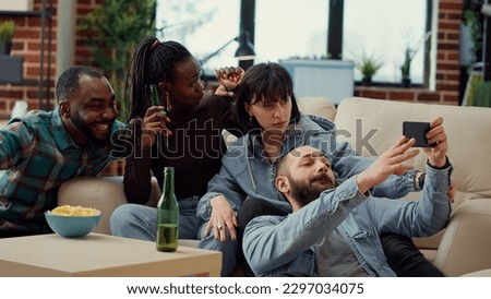 Group of friends taking picture on mobile phone app, having fun with photos at house party with beer bottles. Taking selfies and making memories with internet smartphone. Handheld shot.