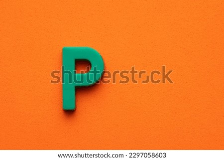 Alphabet letter P - Green plastic piece on orange foamy background