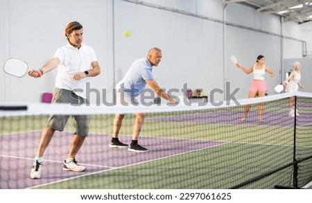 Athletic men playing pickleball tennis on the pickleball court indoors Royalty-Free Stock Photo #2297061625