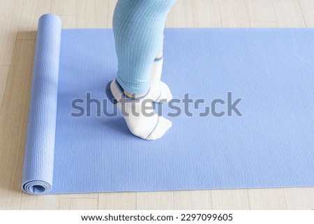 Female legs doing exercises lifting on toes close up on blue background. Royalty-Free Stock Photo #2297099605