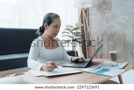 Confident asian chinese mature businesswoman working with laptop and desktop computer doing some paperwork at office workplace. Royalty-Free Stock Photo #2297123691