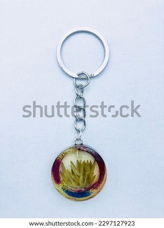 A circle shape keytag on white background.Inside of the keytag has dry leaves.This keytag has silver colour keychain and different colour border.This keytag is made of resin material.it is beautiful.