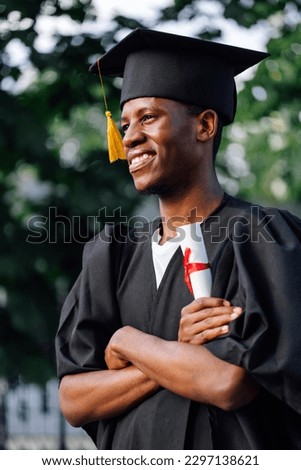 Portrait side view of happy African graduate from university stand outdoors with crossed arms and holding higher education diploma, selective focus. Student, graduation, ceremonial celebration. Royalty-Free Stock Photo #2297138621