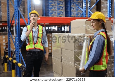 Group of warehouse workers with hardhats and reflective jackets wrapping boxes in stretch film parcel on pallet while control stock and inventory in retail warehouse logistics distribution center