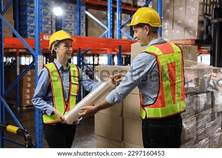 Group of warehouse workers with hardhats and reflective jackets wrapping boxes in stretch film parcel on pallet while control stock and inventory in retail warehouse logistics distribution center