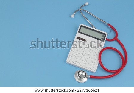 Price of medicine concept. Red stethoscope and white calculator on blue background. Copy space for text.