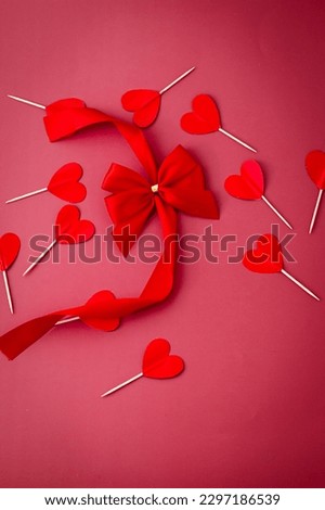 Valentine's inspiration - paper hearts on toothpicks with a bow on a red background.