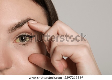 Woman checking her health condition on light grey background, closeup. Yellow eyes as symptom of hepatitis Royalty-Free Stock Photo #2297213589