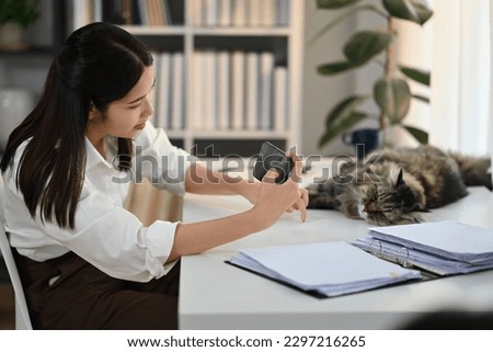 Shot of happy millennial woman using smartphone take a picture with her cat in the home office