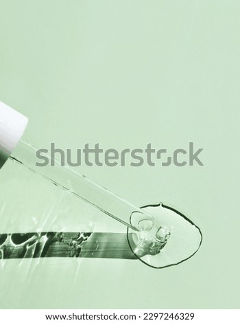 A drop of aloe vera gel and a glass pipette on a green background.