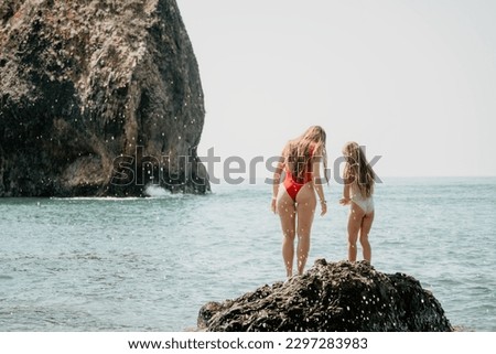 Woman and her daughter practicing balancing yoga pose on one leg up together on rock in the sea. Silhouette mother and daughter doing yoga at beach