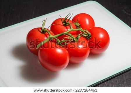It is a branch of cherry tomatoes is on white plastic cutting board. Dark food photography of cherry tomatoes.