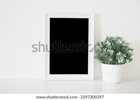 close up of white wooden frame and artificial flower in pot on shelf and  white concrete wall background with clipping path 