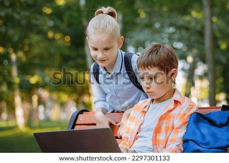 cute caucasian boys sitting on bench in park with laptop computer .Doing homework outdoors after school