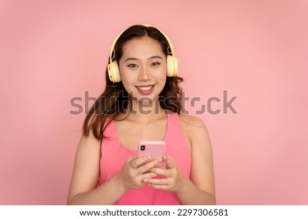 Smiling woman holds a pink smartphone in her hand against a matching background.
