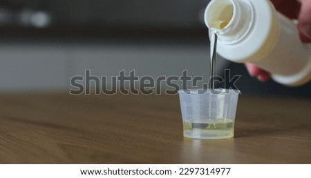 Man pours medical syrup into measuring cap. Medicine syrup bottle. Healthcare, people and Medicine concept. Close-up. Royalty-Free Stock Photo #2297314977