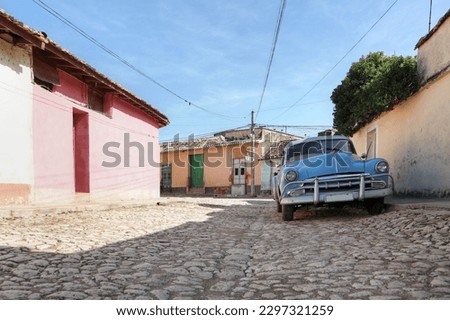 A photo of a light blue old American car using as a Cuban taxi parked on the street of Trinidad with the sky in the background 