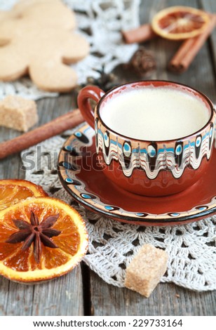 Hot cocoa in a old ceramic cup on a wooden table with pieces of sugar, cinnamon sticks and candied orange slice. Selective focus on milk froth, toned