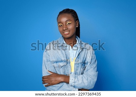 Portrait of cheerful happy beautiful african american young lady 20s on blue studio background, black lady in stylish casual outfit posing with hands crossed on chest, smiling at camera, copy space