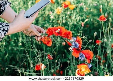 A woman takes a photo on her mobile phone of a wreath of wildflowers, red poppies and blue cornflowers