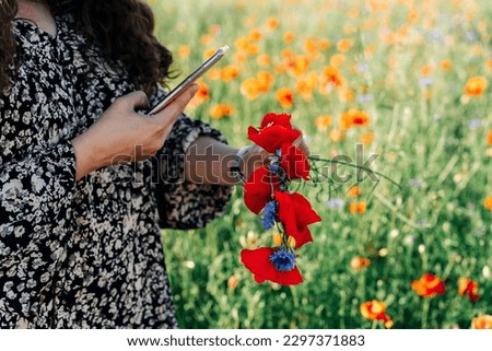 A woman plus size photographs using a phone wreath of wildflowers: red poppies and blue cornflowers