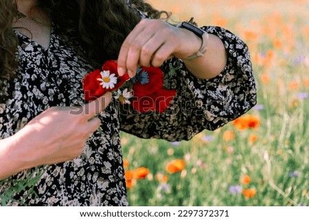Close-up of women's hands weaving a wreath of poppies, daisies and cornflowers.