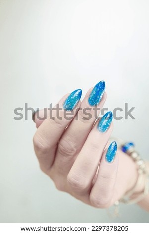 Woman's beautiful hand with long nails and blue manicure with bottles of nail polish