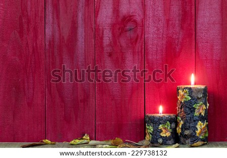Textured fall candles with leaves burning by antique rustic red wood background; blank wooden autumn background with red copy space