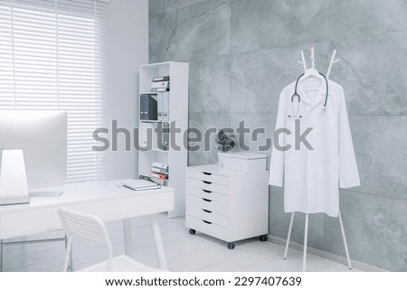 White doctor's gown and stethoscope hanging on rack in clinic Royalty-Free Stock Photo #2297407639