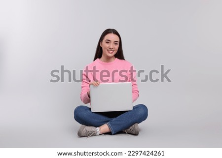 Smiling young woman with laptop on grey background