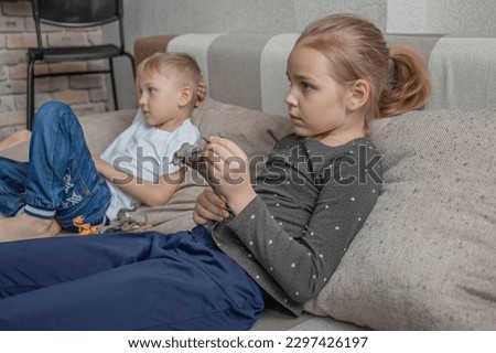 Little brother and sister watch TV together sitting on the sofa in the living room. Interesting and educational programs, videos and cartoons for primary school children.