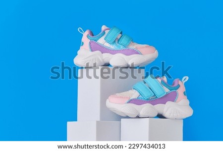 Baby sneakers, child sport shoes pair on blue background. Fashion kids outfit. Fashionable sports shoes. Modern minimalistic layout with footwear mock up for your design. Advertising for shoe store