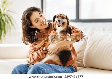 happy cheerful woman hugging her beloved pet dog at home on the couch Royalty-Free Stock Photo #2297436877