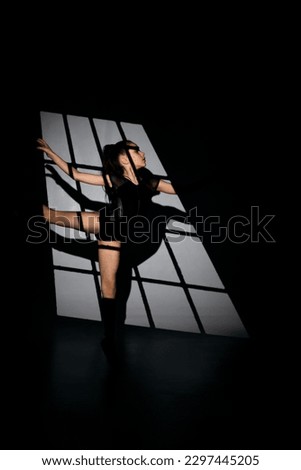 Ballet concept. A girl in a black gymnastic leotard in a beautiful graceful pose on a white background in pointe shoes. Black and white picture. Front view