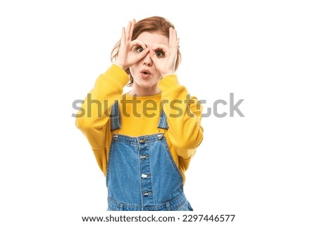 Portrait of young redhead girl making glasses mask with fingers, grimacing isolated on white background