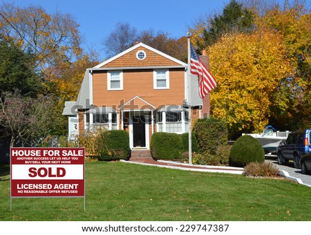 American Flag pole Real Estate Sold (another success let us help you buy sell your next home) sign on front yard lawn of suburban house in residential neighborhood clear blue sky USA