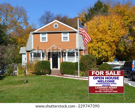 American Flag pole Real Estate For Sale sign on front yard lawn of suburban house in residential neighborhood fall season clear blue sky USA